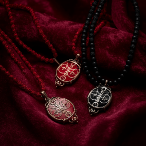 Detalhe elegante de guias (colares) sagradas de Umbanda com contas nas cores vermelho e preto. As guias repousam sobre um tecido escuro aveludado sob uma iluminação dramática que transmite força, segurança e respeito. A imagem ilustra o significado do vermelho (vitalidade) e do preto (absorção de negatividade) no estudo das cores na Umbanda, representando a proteção de Exu e Pombagira.