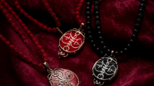 Detalhe elegante de guias (colares) sagradas de Umbanda com contas nas cores vermelho e preto. As guias repousam sobre um tecido escuro aveludado sob uma iluminação dramática que transmite força, segurança e respeito. A imagem ilustra o significado do vermelho (vitalidade) e do preto (absorção de negatividade) no estudo das cores na Umbanda, representando a proteção de Exu e Pombagira.